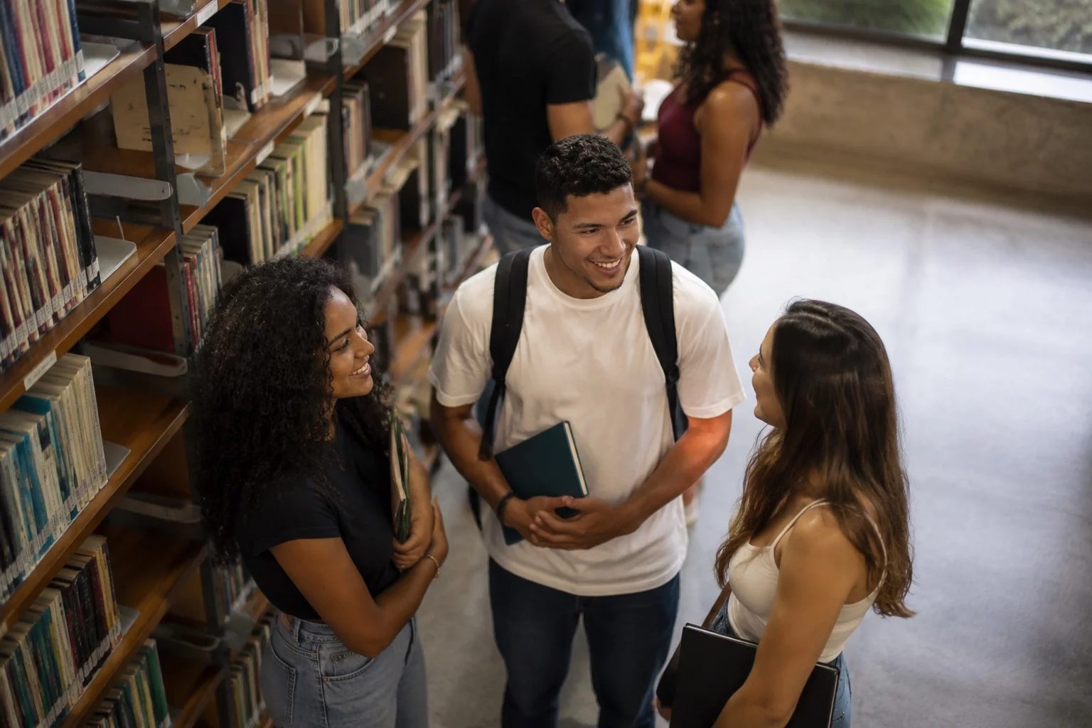 Estudantes conversando em pé entre as estantes de uma biblioteca